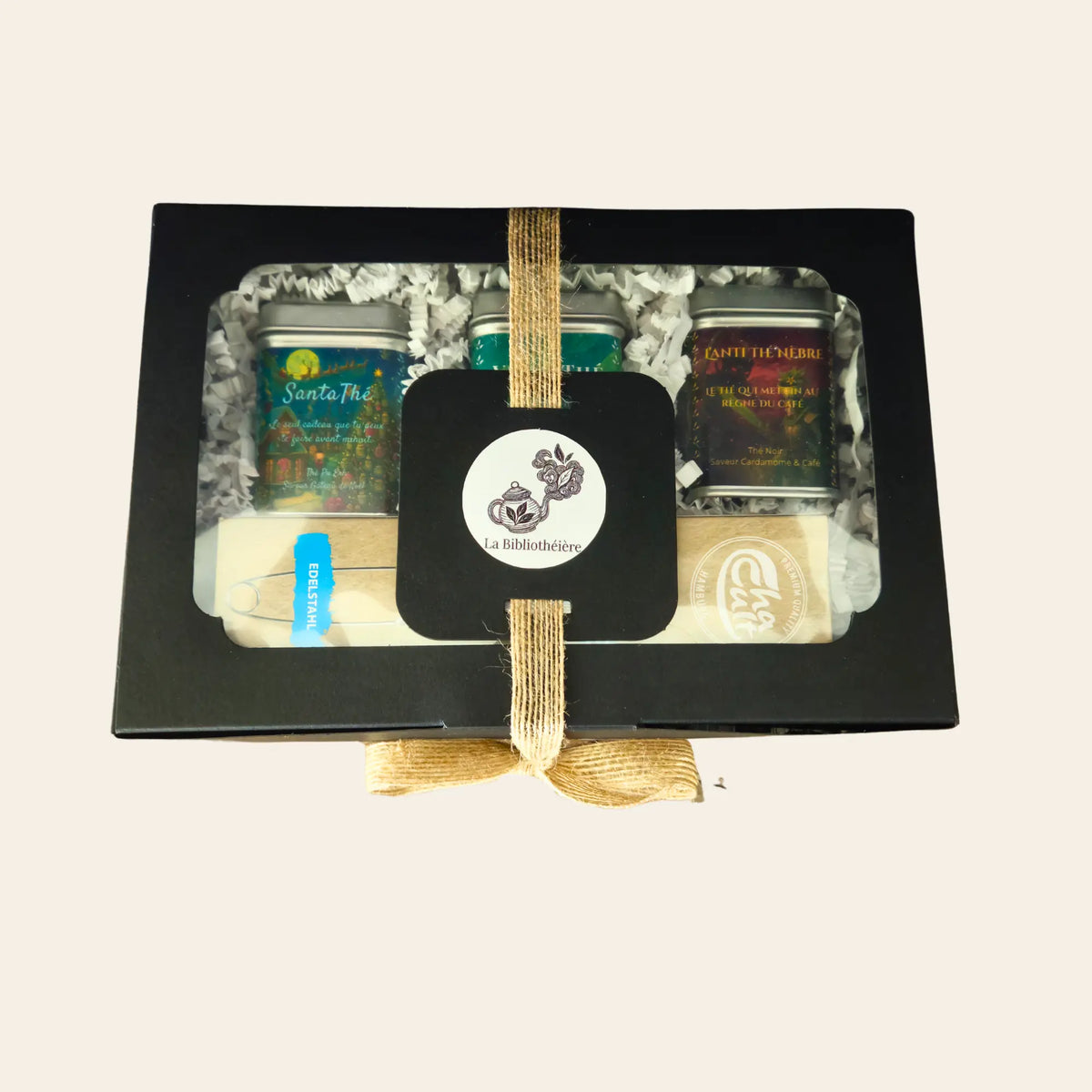 Coffret cadeau La Bibliothéière fermé vu de face, ruban en jute, trois thés en vrac (SantaThé, VitaliThé, L'Anti Thé Nèbre) et une pince à thé