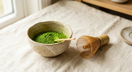Poudre de matcha vert vif dans un bol à côté d'un fouet en bambou, sur fond crème