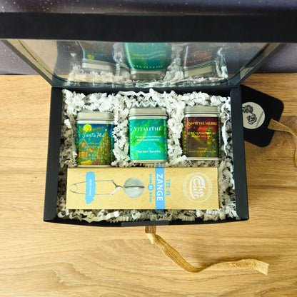 Coffret cadeau La Bibliothéière ouvert vu de dessus, trois boîtes de thé en vrac (SantaThé, VitaliThé, L'Anti Thé Nèbre) et une pince à thé inox posée sur son étui